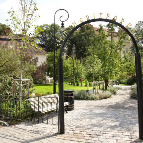 An iron gate leading into the park, where paths, trees and lawns can be seen