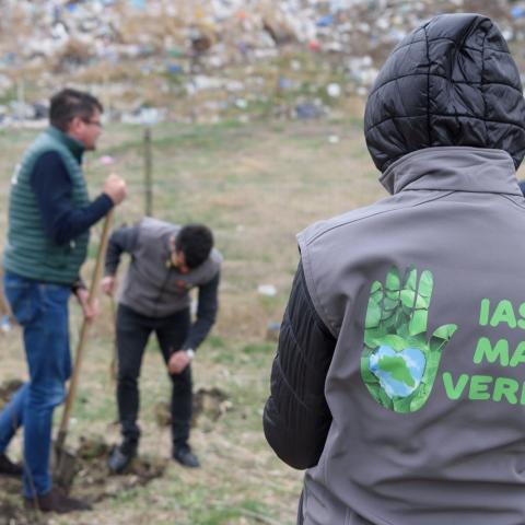 Back with shirt with logo of the campaing, volunteers planting in the background 
