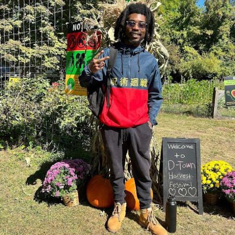 Man posing with welcome to D-town Farm harvest festival sign